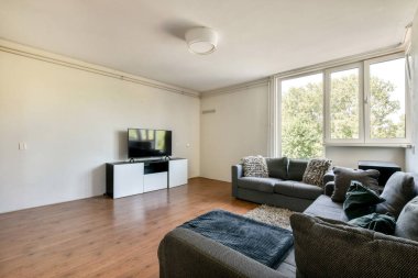 Rahat bir kanepe, gösterişli bir dolap üzerinde televizyon ve doğal ışık getiren büyük pencereli modern bir oturma odası..