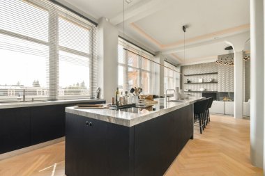 Geniş, modern mutfak. Parlak bir dolap, büyük bir ada ve geniş pencerelerden süzülen bol miktarda doğal ışık. Sıcak bir ortam yaratıyor..