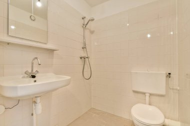 Beyaz fayansların, duşun, lavabonun ve tuvaletin olduğu temiz ve minimalist bir banyo. Tasarım, modern yaşam alanları için ideal olan basitlik ve işlevselliği vurgular..
