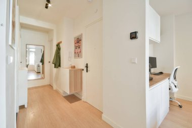 Şık ve minimalist bir koridorda bir çalışma alanı, bir sandalye, dekoratif bir ayna, ve sıcak ahşap döşeme, davetkar bir atmosfer yaratıyor..