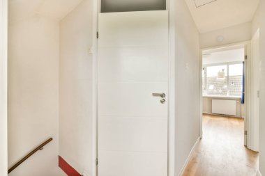 Temiz, modern bir iç koridor. Beyaz bir kapı ve parlak ahşap döşeme, yaşam alanında parlak ve davetkar bir atmosfer yaratıyor..