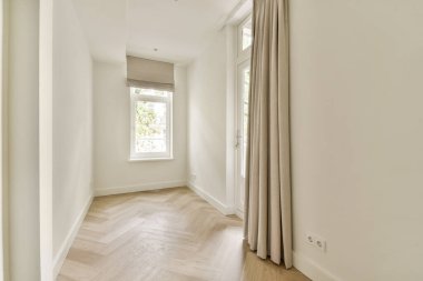 Basit tasarım elementlerinin, büyük pencerelerden akan doğal ışığın ve zarif bej perdelerin bulunduğu sakin ve aydınlık bir oda..