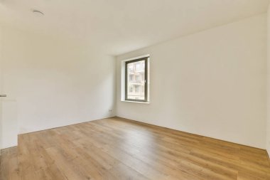 Geniş, modern bir iç mekan. Temiz hatları ve parlak ahşap döşemeleri var. Oda büyük bir pencereden içeri giren doğal ışıkla aydınlık..