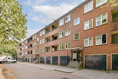 Çağdaş mimari ve kentsel yaşamın sergilendiği, birden fazla kat, büyük pencere ve çevreleyen ağaçların yer aldığı modern bir apartman kompleksi..