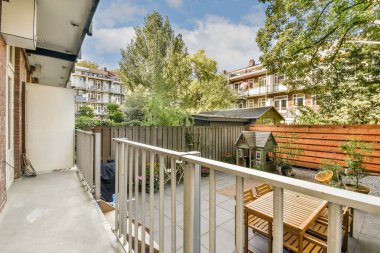 Bereketli yeşillik ve kentsel mimari içeren sakin bir balkon manzarası. Canlı bir şehirde rahatlamak ve doğanın tadını çıkarmak için mükemmel..