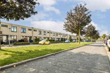 Düzenli evler, ağaçlar ve park edilmiş arabaların yer aldığı modern bir yerleşim yeri manzarası, sakin bir banliyö ortamı sergiliyor..
