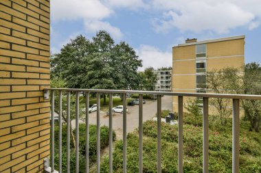 Sergilenen bir balkondan manzara yeşillik, konut binaları, ve huzurlu bir ortam, rahatlamak ve doğanın tadını çıkarmak için ideal..