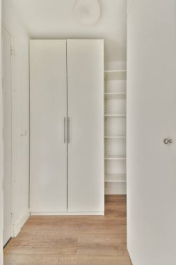 Parlak ve havadar bir oda, parlak beyaz bir gardırop, parlak ahşap döşemeler, modern bir estetik için minimalist iç tasarım ilkeleri sergiliyor..