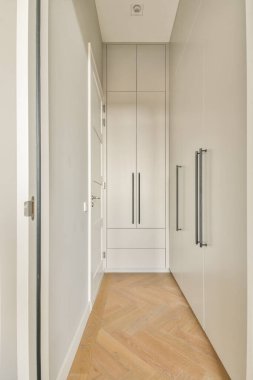 Temiz, modern bir koridor, gösterişli dolaplar ve sıcak ahşap döşemeler. Tasarım, nötr renkler ve düz çizgilerle minimalizmi vurguluyor..