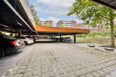 Sanatsal mimari ve ağaçlar gibi doğal elementlerin kombinasyonu ile tasarlanmış geniş, modern bir park alanı, görsel olarak çekici bir ortam yaratıyor..