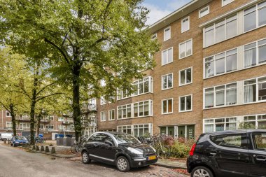 Park halindeki arabaların ve bereketli ağaçların yer aldığı modern şehir manzarası, doğa ve şehir mimarisinin karışımını vurguluyor..