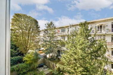 Çağdaş apartman binalarıyla çevrili bereketli ağaçlar ve renkli bitkilerin karışımından oluşan parlak bir şehir avlusu, şehirde doğaya bir bakış sunuyor..