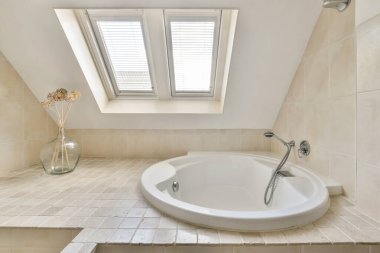 Beyaz bir küvet, nötr fayanslar ve doğal ışık getiren bir tavan penceresi olan geniş ve zarif bir şekilde tasarlanmış bir banyo..