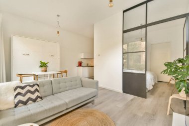 Zarif ve modern bir oturma odası şık gri bir kanepe, minimalist bir dekor ve parlak doğal ışık, sıcak ve davetkar bir atmosfer yaratıyor..