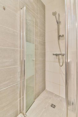 Duş kabini olan bir banyo ve sol tarafında tuvalet kağıdı olan beyaz bir kiremit var.