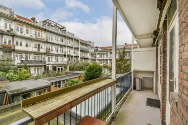 Çağdaş ve klasik mimari tarzları yeşillikler arasında harmanlayan, birden fazla meskun binaya bakan sakin bir balkon manzarası..