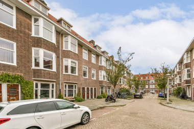 Modern binalar, ağaçlar ve park halindeki arabalarla dolu bir yerleşim yerinin manzarası canlı bir şehir atmosferi sergiliyor..