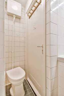 Duvarlarında fayans döşemesi ve duvar kiremitleri olan küçük bir banyoda beyaz bir tuvalet var.