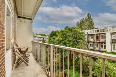 Arka planda sandalyeler ve ağaçlarla dolu bir balkon. Güneşli bir gün fotoğrafı. Gün batımında bir apartmanın balkonundan çekilmiş.