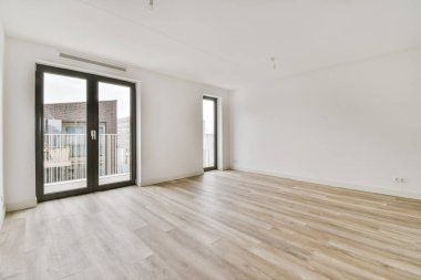 Parlak boş bir odanın içinde balkona açılan kapılar var.