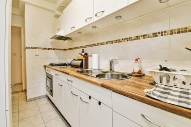 Resmin ortasında beyaz dolaplar ve ahşap tezgahlı bir mutfak başka bir odaya açılan açık bir kapıdır.