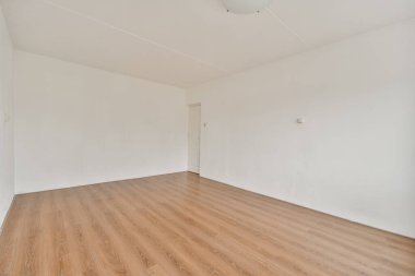 Pürüzsüz ahşap döşeme, beyaz duvarlar ve sakin bir atmosfer sağlayan basit bir tavan ışığı içeren dağınık, minimalist bir iç mekan..