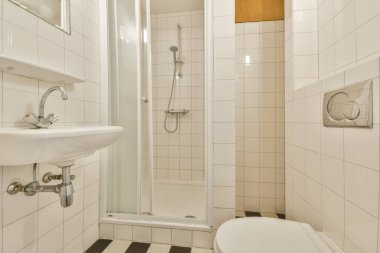 Pürüzsüz, modern bir banyo, küçük bir duş alanı, minimalist lavabo ve şık duvar döşemeleri, temiz çizgiler ve tasarımda işlevselliği vurguluyor..