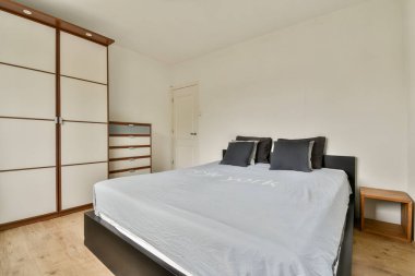 Zarif bir yatak odası, nötr renkli duvarlar, ve düzenli depolama dolabı, sakin ve işlevsel bir alan yaratıyor..