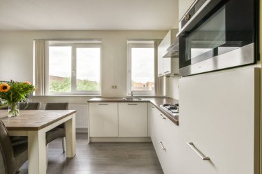 Zarif, modern bir mutfak, gösterişli bir dolap, ahşap bir yemek masası, ve doğal ışıkla alanı genişletecek parlak pencereler..