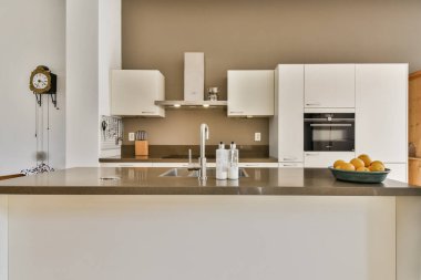 Gösterişli, modern mutfak, beyaz dolaplı minimalist bir estetik, basit bir tezgah, ve taze meyve sergisi, temiz ve davetkar bir alan yaratıyor..