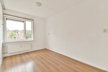 Geniş pencereli, ahşap döşemeli ve beyaz duvarlı doğal ışığa izin veren minimalist boş bir oda geniş bir ortam yaratıyor..