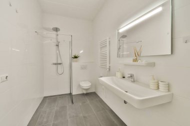 Cam duşlu, modern lavabolu ve zarif dekorlu gösterişli minimalist bir banyo. Tasarım, nötr tonlarla temizlik ve işlevselliği vurguluyor..