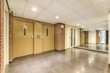 Çağdaş bir asansör lobisi. Parlak duvarlar, cilalı döşemeler ve şık ışıklandırmalar. Bu alan bir sofistike ve işlevsellik hissi taşır..