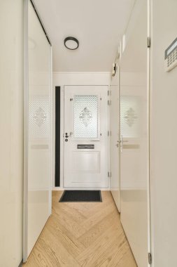 Beyaz bir kapı ve minimalist tasarım unsurlarının yer aldığı gösterişli ve modern bir giriş. Koridor şık bir zemin ile aydınlık, davetkar ve çağdaş.