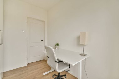 Beyaz bir masa, ergonomik sandalye ve rahatlatıcı ama üretken bir atmosferi hedefleyen ince bir dekor içeren gösterişli ve minimalist bir ev ofisi..