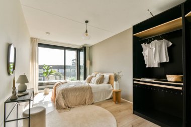 Doğal ışıklandırması, rahat bir yatağı ve minimalist dekoru olan büyük bir penceresi olan şık, modern bir yatak odası. Boşluk temiz çizgileri ve sadeliği vurguluyor..