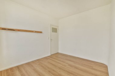 Huzurlu, minimalist boş bir oda beyaz bir duvara karşı ahşap bir askılık ve açık ahşap döşeme, basitliği ve boşluğu vurgulayan.