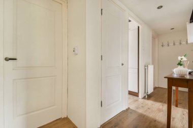 Geniş, aydınlık bir koridor. Parlak beyaz kapılar, açık ahşap döşemeler ve minimalist dekorlar var. Hoş bir atmosfer yaratıyor..