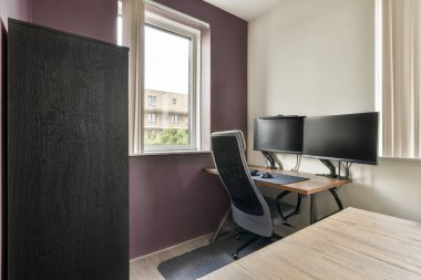 Geniş bir penceresi, bilgisayarlı bir masası ve minimalist dekoru olan gösterişli bir ev ofisi. Doğal ışık üretkenlik için çalışma alanı atmosferini artırır.