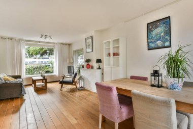 Ahşap döşeme, şık mobilyalar ve doğal ışık getiren geniş pencereli rahat ve modern bir oturma odası rahatlama için sıcak bir atmosfer yaratıyor..