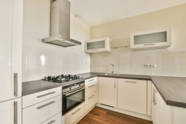 Gösterişli dolaplar, gaz sobası ve minimalist tasarım elementlerinin yer aldığı şık bir modern mutfak. Uzay, tam bir görünüm için işlevsellikle çağdaş estetiği harmanlıyor.