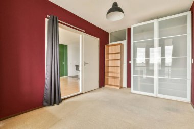 Geniş ve modern boş bir oda, kırmızı duvarlar, minimum mobilyalar, ve basit bir aydınlatma armatürü, temiz ve davetkar bir atmosfer yaratıyor..