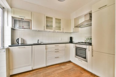 Beyaz dolapların, siyah tezgahların ve modern aletlerin yer aldığı şık bir mutfak, temiz ve çağdaş bir tasarımı vurguluyor..