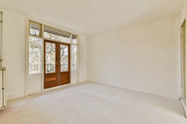 Doğal ışığın içeri girmesini sağlayan geniş pencereli boş bir oda. Minimalist tasarım, bölgenin genişliğini vurgular..