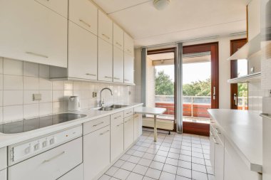 Parlak ve ferah bir mutfak. Parlak beyaz dolaplar, fayanslı zemin ve açık hava manzarası sunan büyük pencereler..