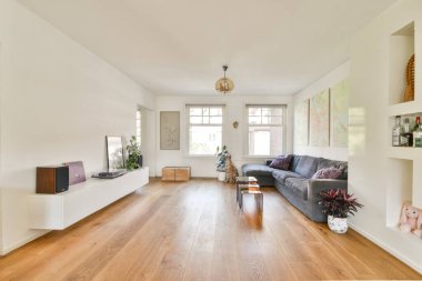 Minimalist dekorun, doğal ışığın ve zarif döşemelerin olduğu geniş, modern bir oturma odası. Ahşap zemin ve canlı sanat eserleri davetkar atmosferi güçlendirir..