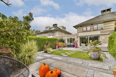 Canlı balkabaklarının, yemyeşil yeşilliklerin ve berrak mavi gökyüzüne karşı modern konutların bulunduğu güzel manzaralı bir bahçe, huzur ve sükunetin vücut bulmuş hali..