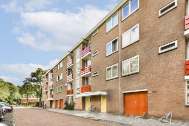Geniş pencereli ve canlı yüzlü çağdaş kırmızı tuğlalı bir apartman kompleksi. Çevresi yeşilliklerle çevrili, modern şehir yaşamını somutlaştırıyor..