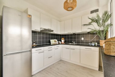 Beyaz dolaplar ve koyu dokuların karışımından oluşan gösterişli ve şık bir mutfak. Yeşillik ve çağdaş aydınlatma armaşıklarıyla tamamlanmış..