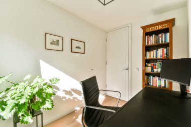 Parlak ve davetkar bir ev ofisi. Parlak bir sandalye, saksı çiçeği ve atmosferi güçlendiren sıcak doğal ışıklandırması olan iyi düzenlenmiş bir kitaplık..